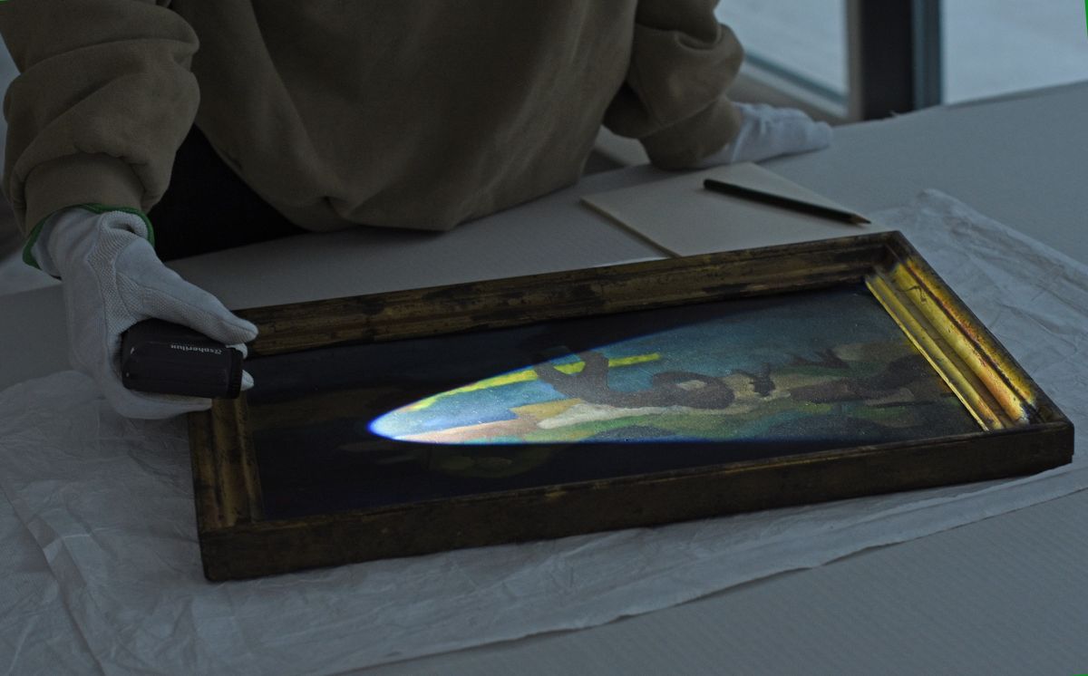 In abgedunkelter Umgebung untersucht eine Person mit einem LED-Handstrahler ein Gemälde